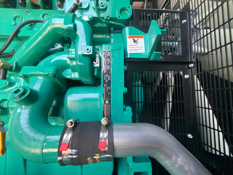 Load image into Gallery viewer, A close-up of a Cummins industrial engine with a curved gray metal pipe secured by black hose clamps, alongside a black protective mesh guard and a warning label.
